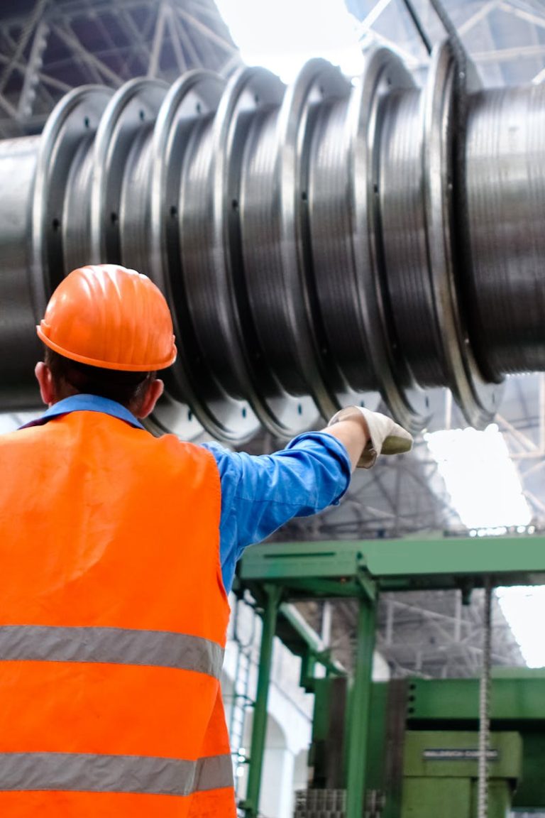 Engineer in high visibility vest and hard hat inspecting large machinery in factory setting.